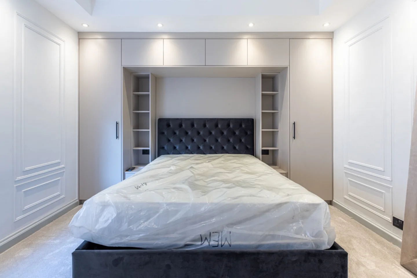 Fitted bedroom closet in soft grey wrapping the bed, with LED-lit open shelving and a tufted velvet headboard