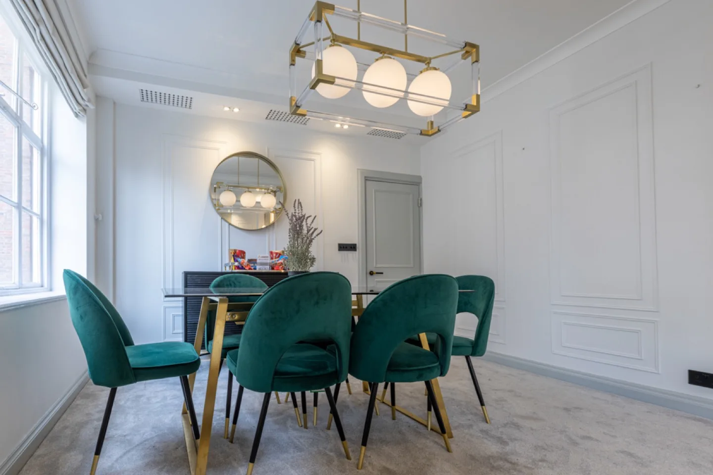 Dining room with floor-to-ceiling decorative wall panelling, green velvet chairs and a brass globe pendant light