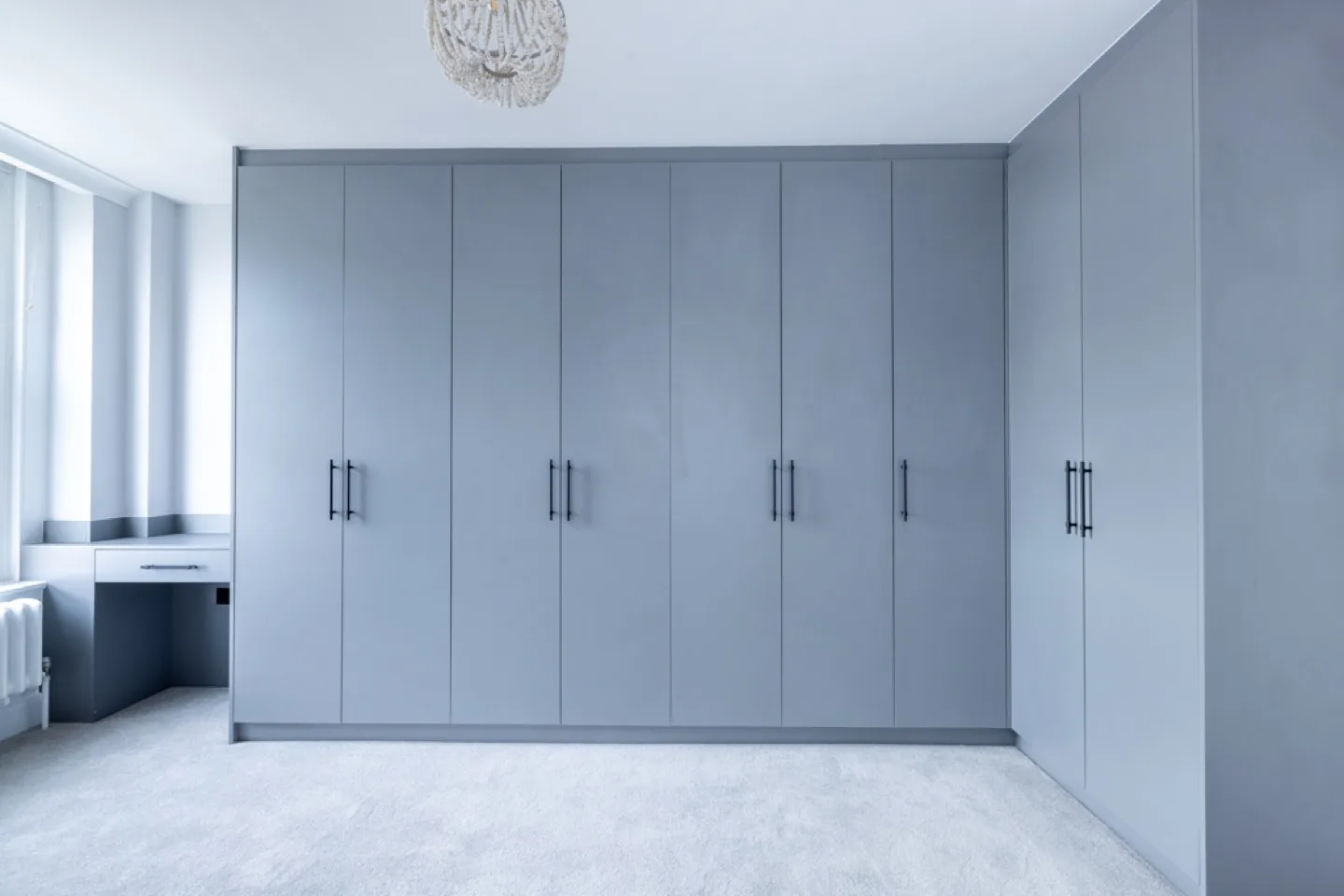 Master bedroom wall of grey fitted wardrobes with black bar handles and a built-in dressing nook