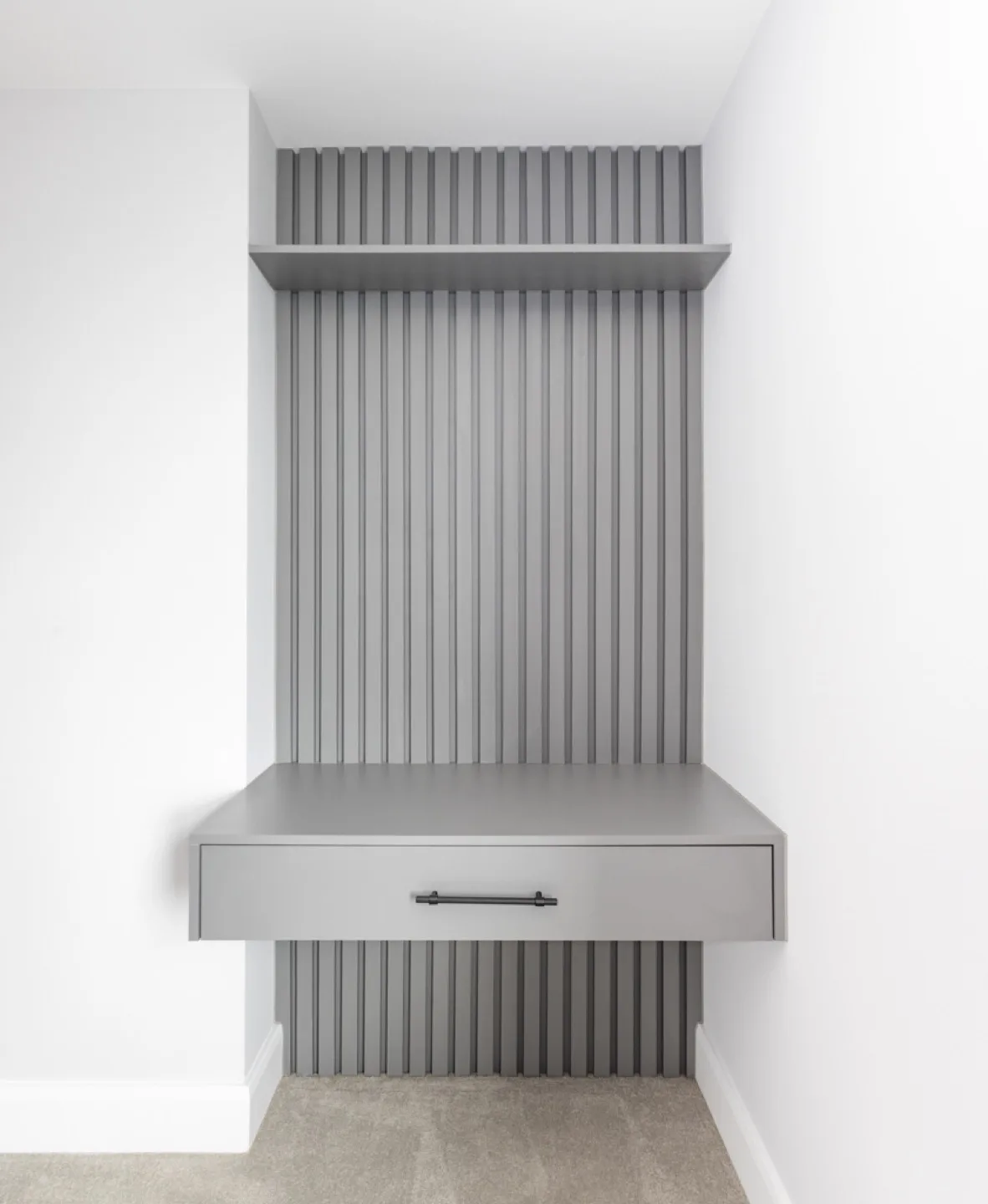 Floating grey desk with a drawer set against grey slatted panelling, with a display shelf above