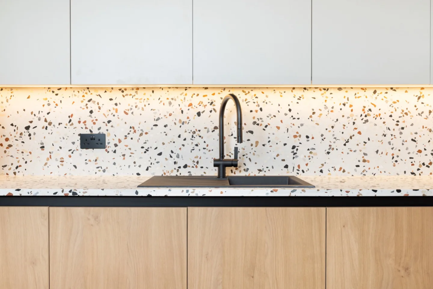 Terrazzo worktop and splashback with black undermount sink and tap above oak base units
