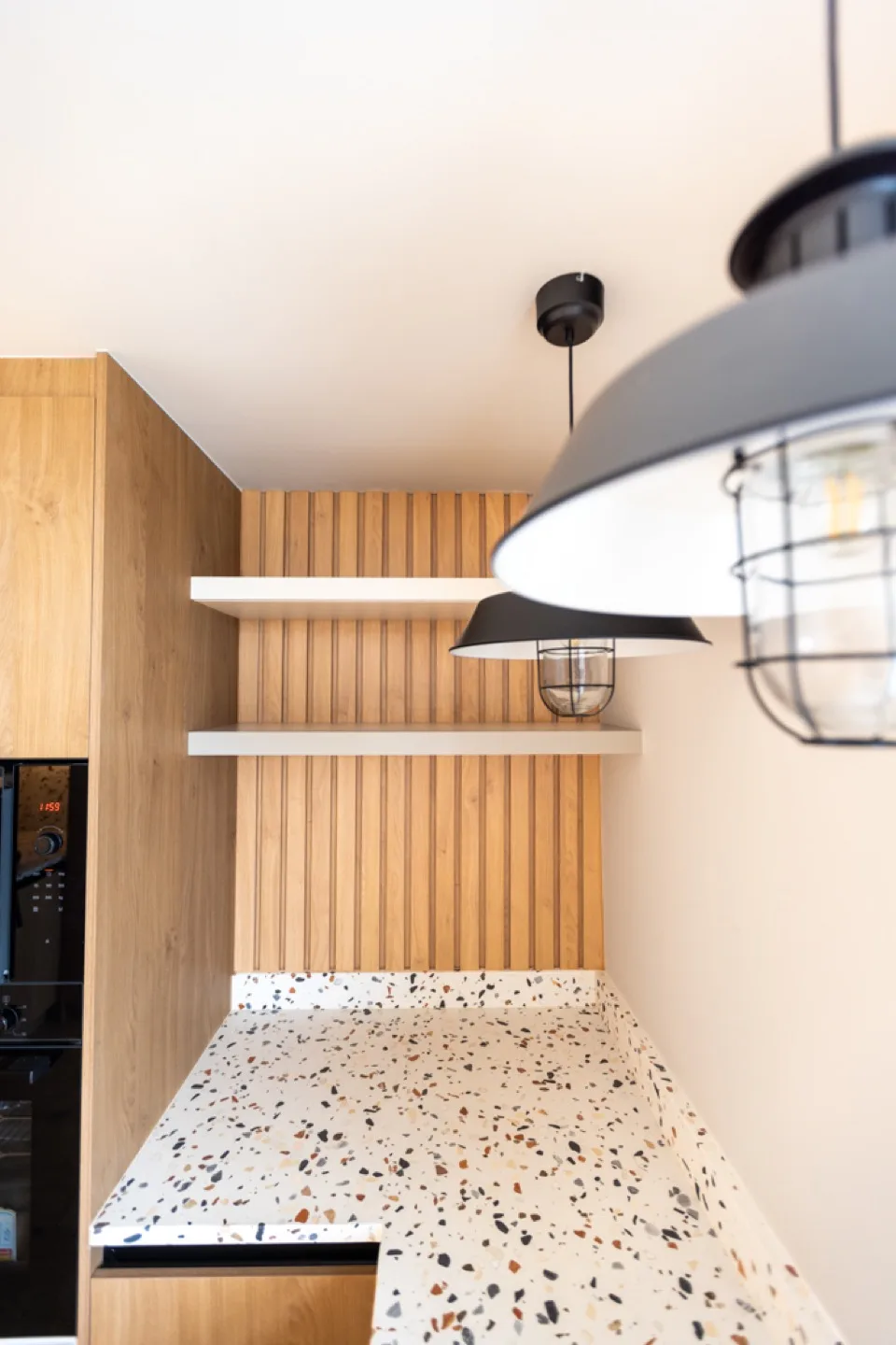 Oak slatted alcove with white floating shelves above a terrazzo worktop and black pendant lights