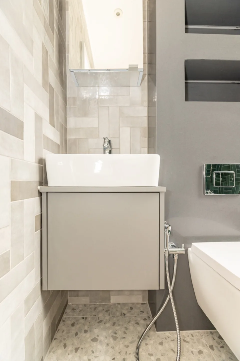Bespoke grey wall-hung vanity unit with a white countertop basin against herringbone tiling