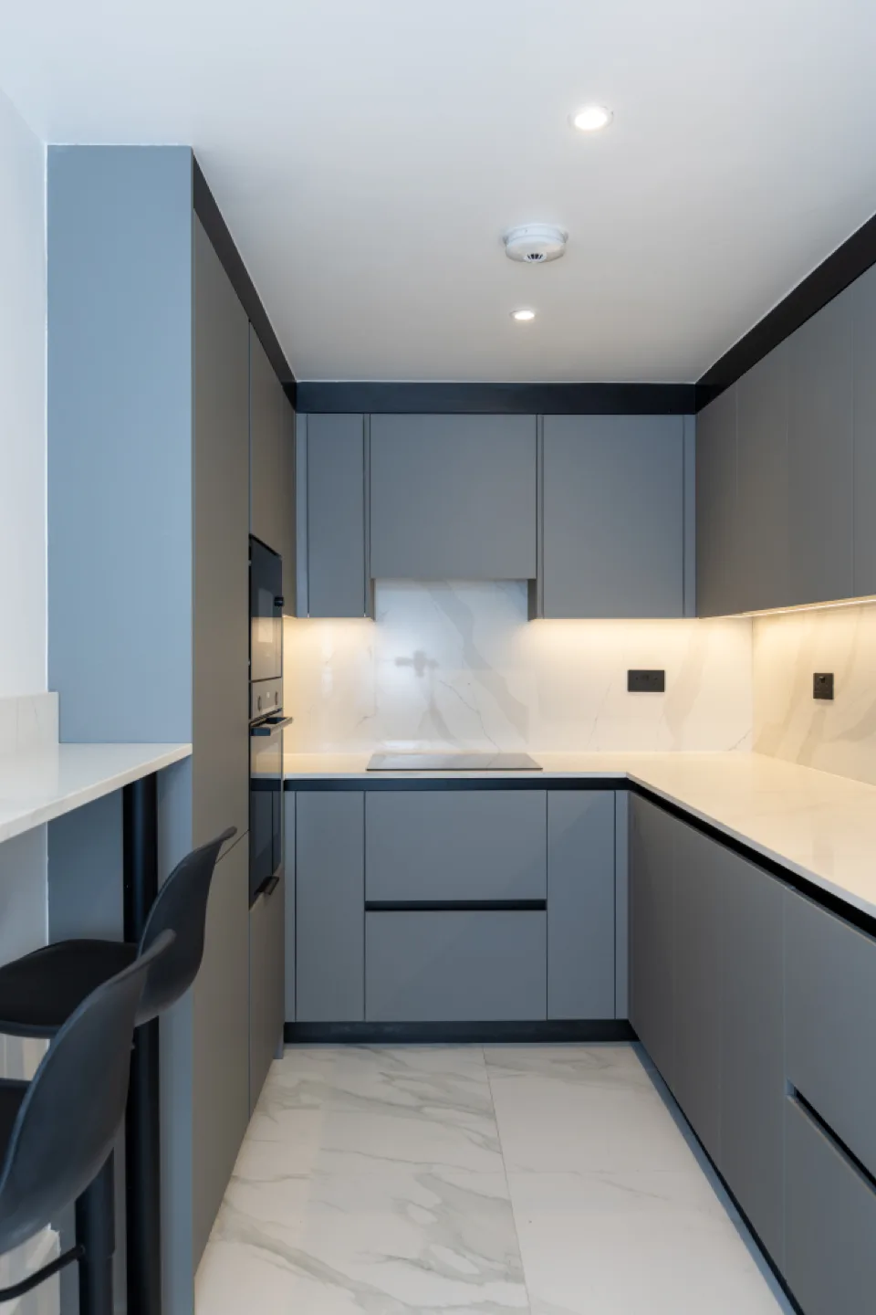 U-shaped grey kitchen with integrated black oven and microwave, induction hob and marble quartz splashback