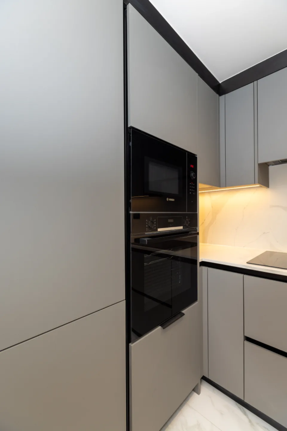 Tall grey larder units housing an integrated Bosch oven and microwave, lit by warm undercabinet lighting