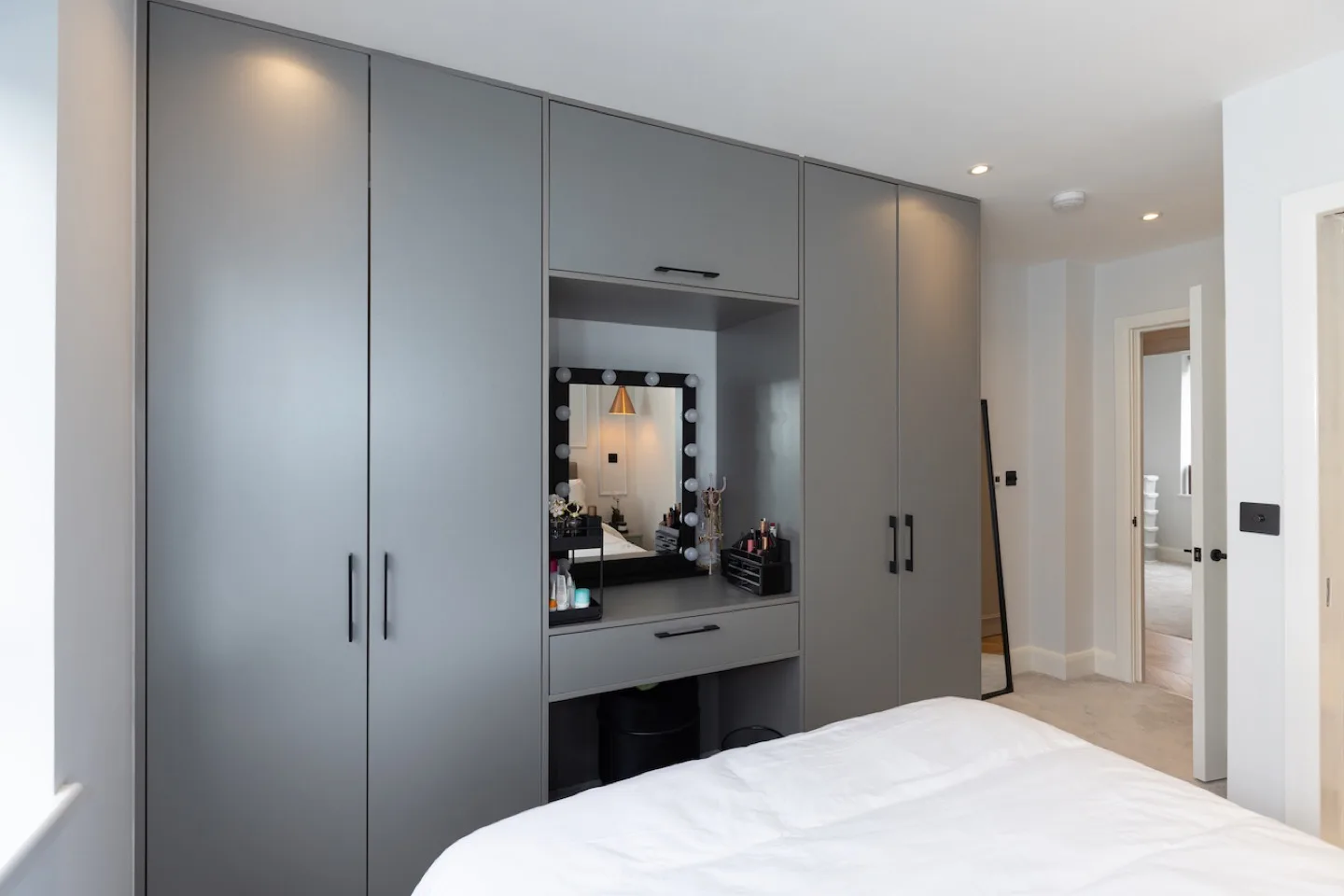 Grey fitted bedroom wardrobes with a built-in dressing station and Hollywood-style lit mirror