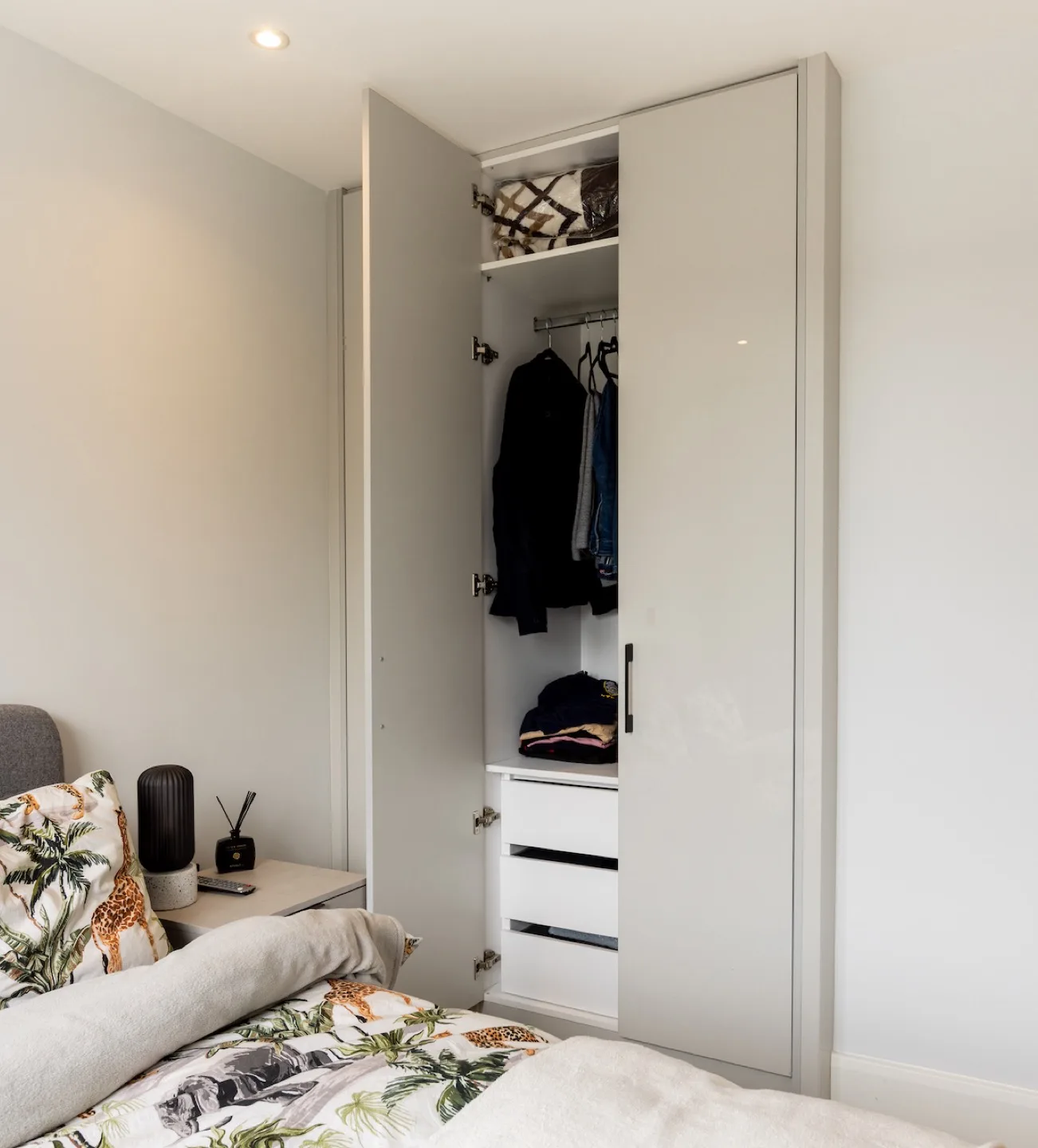 Fitted guest wardrobe open to show hanging rail, top shelf and internal drawers full of clothes