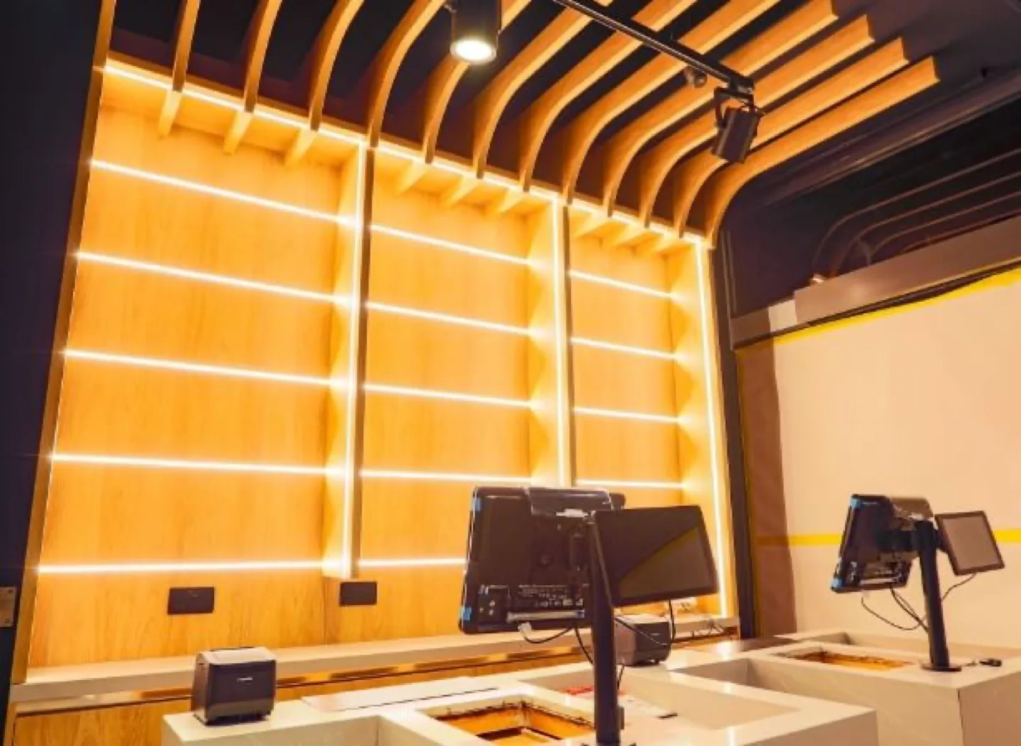 Curved oak-slat ceiling above an LED-lit display wall behind the till