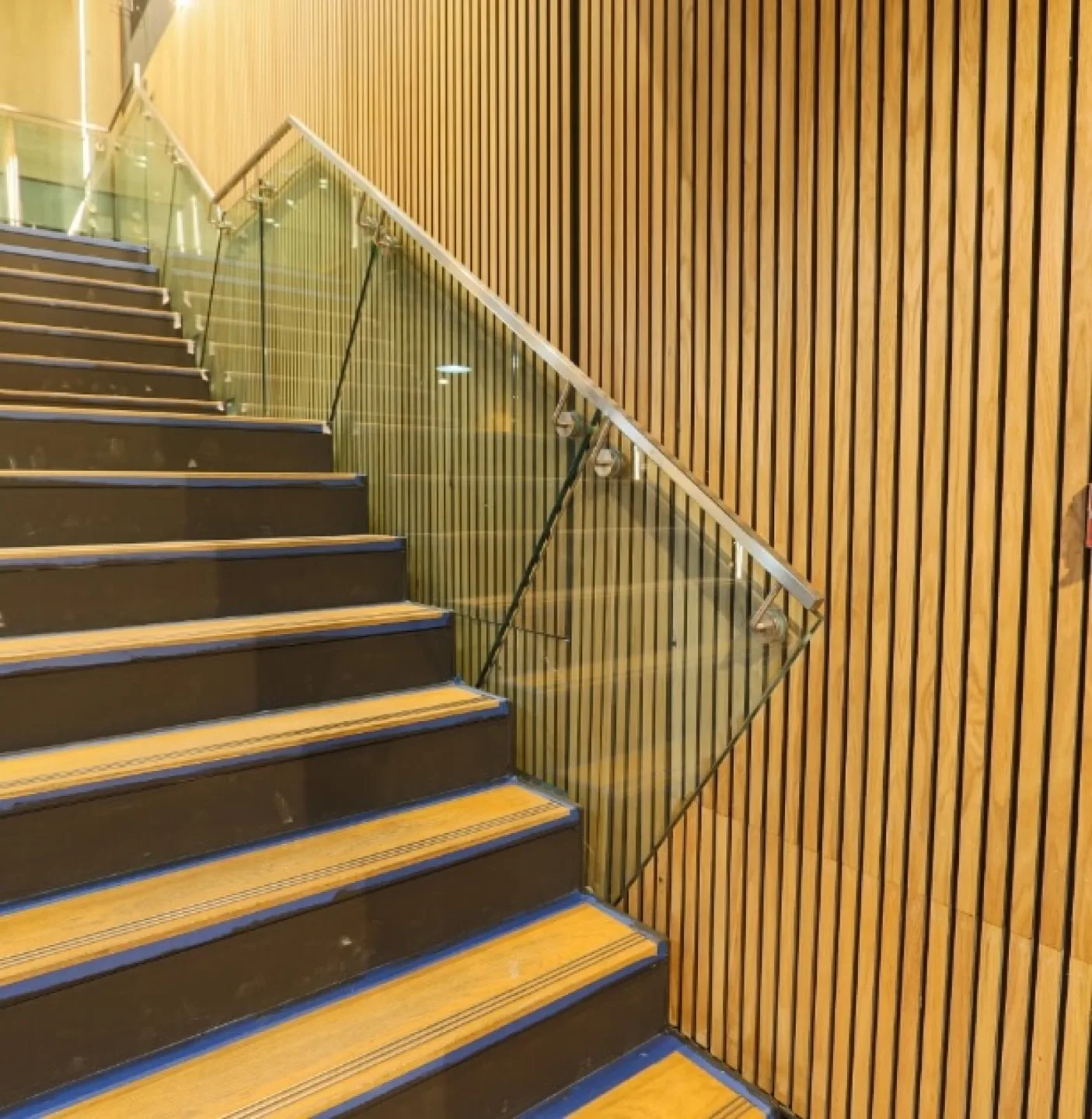 Oak-slat clad wall running alongside a staircase with glass balustrade