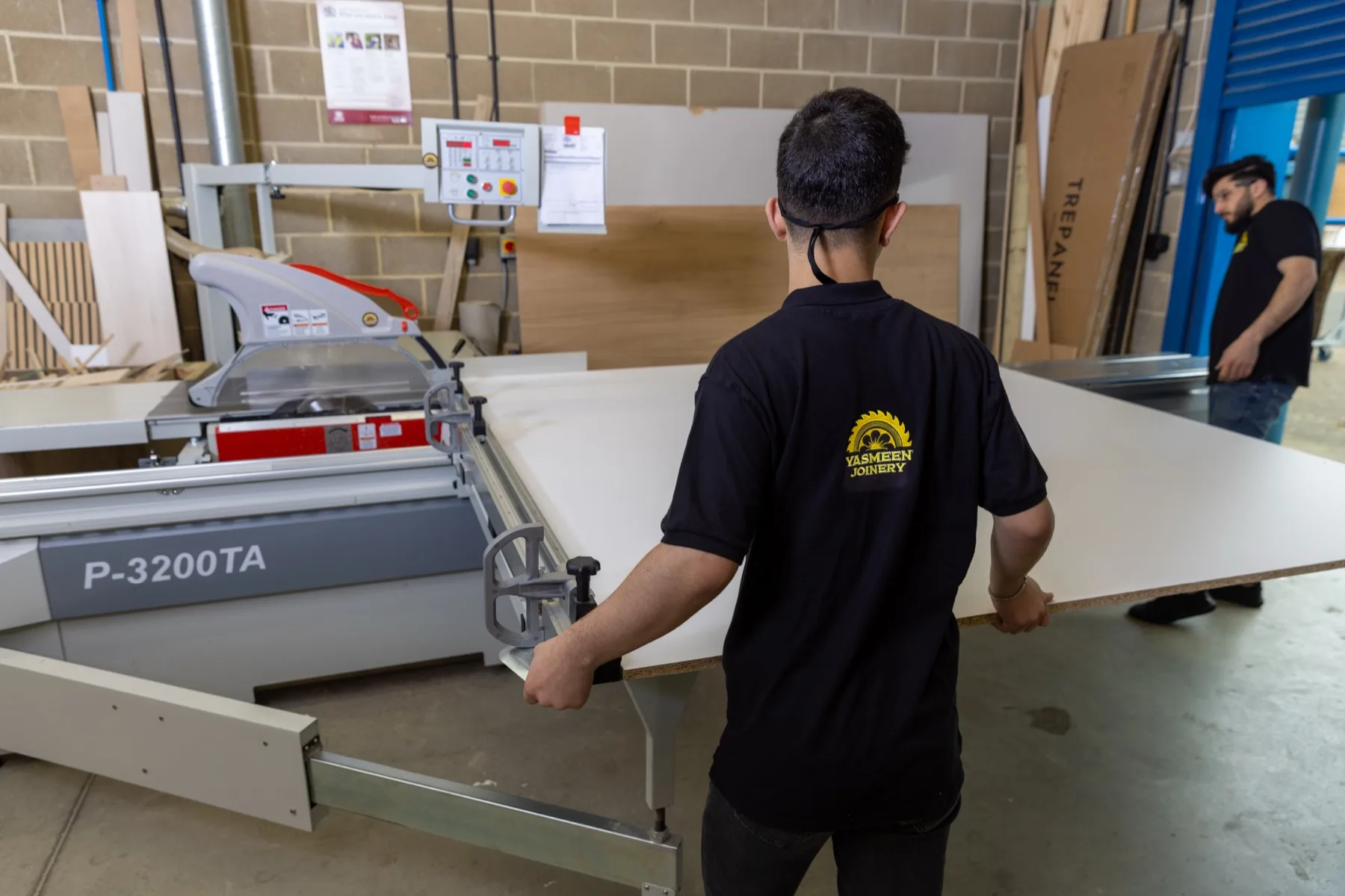 Two team members carrying a board across the workshop