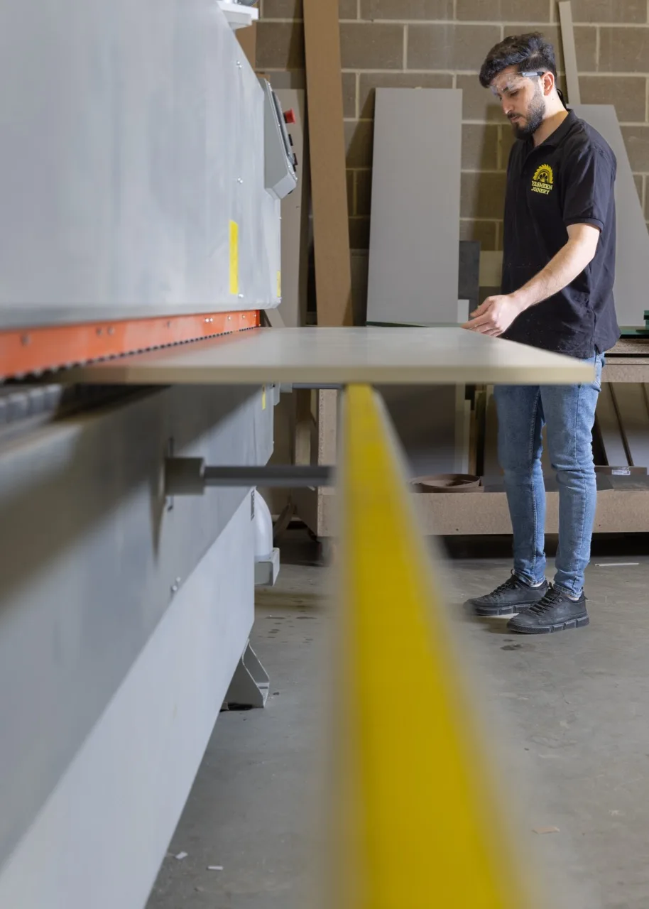 A craftsman feeding board through the edge bander in the Yasmeen Joinery workshop